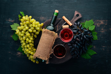 Red wine in a bottle with a glass and grapes. On a black wooden background. Free space for text. Top view.