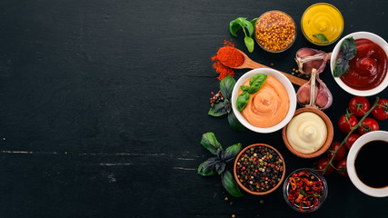 Set the sauces on a black wooden background. Ketchup, mayonnaise, mustard, soy sauce, barbecue sauce, pepper and spices. Top view. Free space for text. - obrazy, fototapety, plakaty