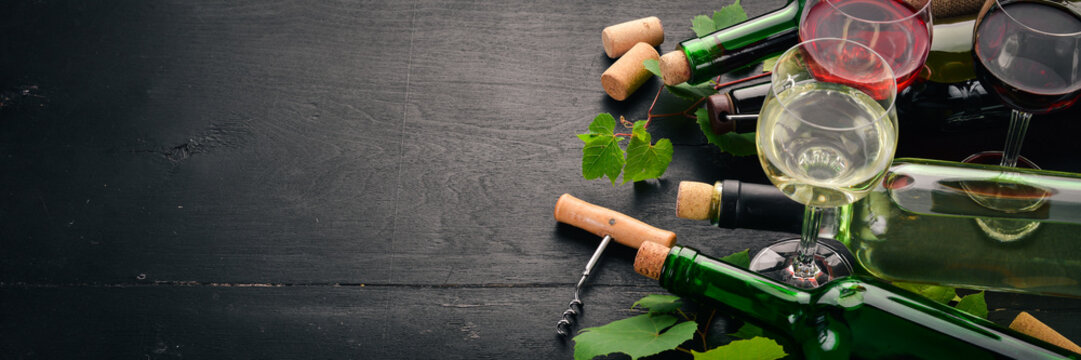 Set of red and white wine in bottles and glasses. Grape. On a black wooden background. Free space for text. Top view.