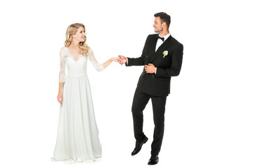 smiling young bride and groom holding hands and looking at each other isolated on white
