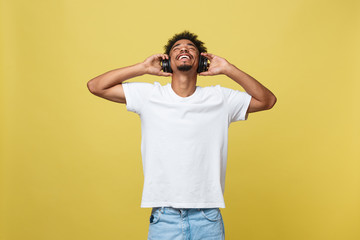 Young African American man wearing headphone and enjoy music over yellow gold Background