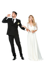shocked young bride looking at camera while groom drinking champagne isolated on white