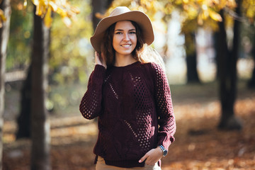 Portrait of happy smile young woman outdoors in autumn park in cozy sweater and hat. Warm sunny weather. Fall concept. Copy space.