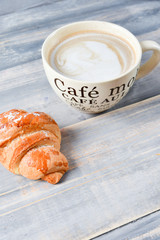  Breakfast is a large beige Cup of coffee with milk and croissants on a wooden table. on the Cup inscription in French (top down: mocha coffee, coffee with milk, coffee without sugar)
