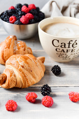 Breakfast at the European hotel: coffee with milk and croissants, jam and fresh raspberries and blackberries on a wooden table. on the Cup inscription in French (mocha coffee, coffee with milk)
