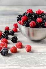 fresh organic blackberries and raspberries in a metal bowl on a wooden table, concept of diet, vitamins and antioxidants. selective focus and copy space