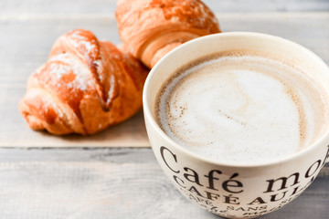  Breakfast is a large beige Cup of coffee with milk and croissants on a wooden table. on the Cup inscription in French (top down: mocha coffee, coffee with milk, coffee without sugar)