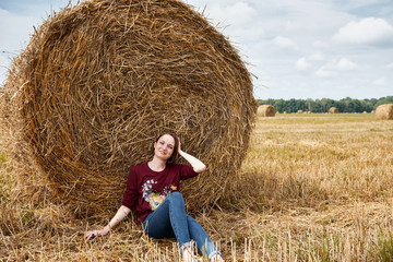 Naklejka na ściany i meble young girl having fun in the field, sits in a haystack and relaxing