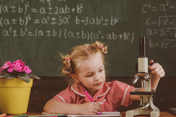 Little girl with microscope in school laboratory. Schoolgirl work with laboratory equipment on...