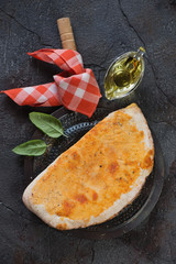 Freshly baked calzone pizza, flatlay over grey cracked stone background, vertical shot