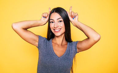Fototapeta premium Young attractive cute brunette woman in gray T-shirt is posing and looking on camera isolated over yellow wall
