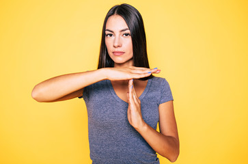 Obraz premium Stop and think. Portrait of young confident beautiful woman in casual wear is doing T symbol or sign with help of her hands and looks on camera