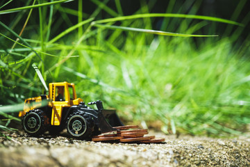 Closeup mini tractor with stack coins on ground using as business, industrial and financial concept