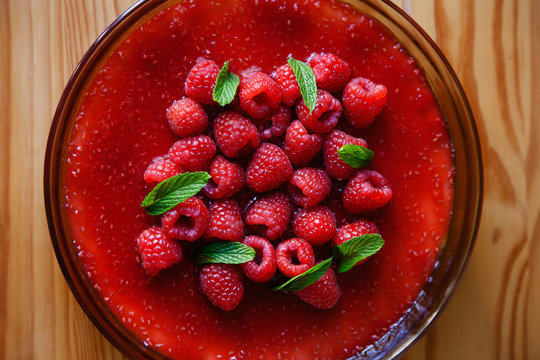 Fresh red raspberry cheesecake with mint on a textured wooden surface