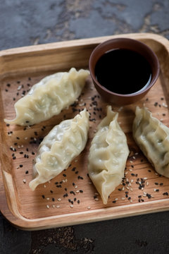Wooden serving tray with steamed korean dumplings and soy sauce, vertical shot, close-up