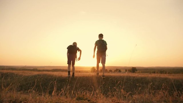 Two travelers boy. Two boys are walking along the field at sunset with rucksacks. The concept of family and travel
