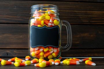 Halloween background frame consisting of a jar full of candy corn on a dark wooden table with a black lable that you can personalize.