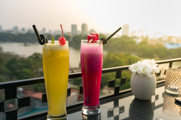Passion fresh fruit juice with ice on outdoor table in cafe and bar. Pineapple and red dragon fruit. Urban lake on background