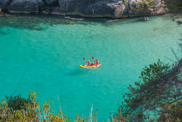 A family on a kayak in the crystalline sea of cove Macarelleta in Menorca
