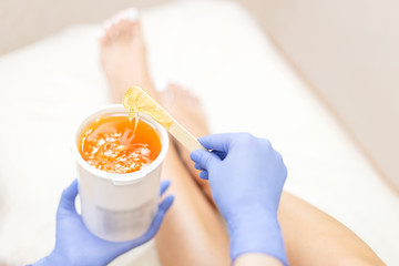 Close-up hands of cosmetologist in blue gloves holding paste for sugaring depilation