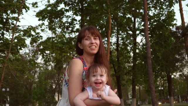 Mom throws child in air on street for fun. Baby laughs at hands of loving mom. Baby and mom laugh, playing together for walk in park.