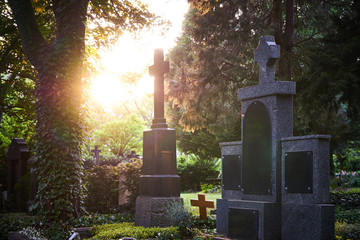 Sunlight shines through the trees of a graveyard touching old tombstones on a graveyard at sunset...