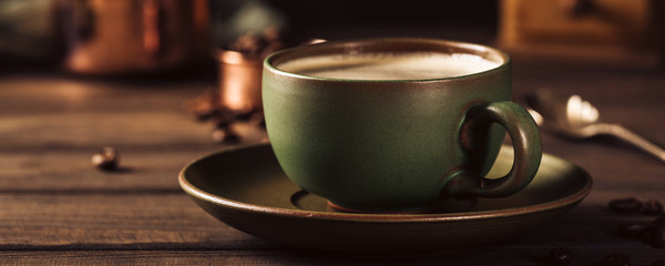 Green cup of coffee with beans and coffee mill on old wooden background with copy space. Retro...