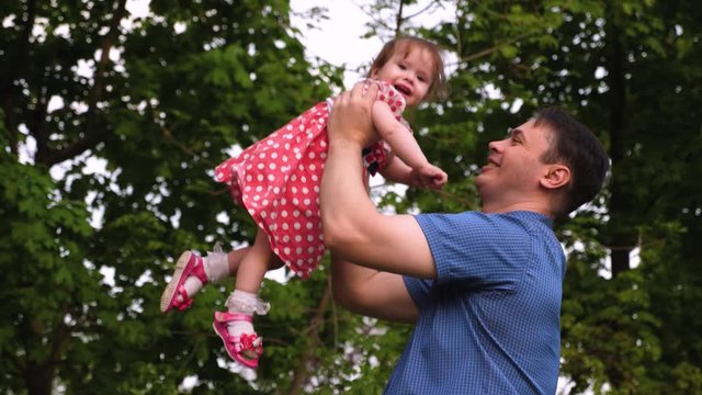 Young dad and baby laughing together while playing outdoors. Girl is jumping in air at hands of parent and smiling. Happy childhood. Slow motion.