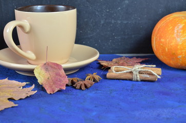 Pumpkin spiced latte or coffee in cup, dry leaves, gifts on dark blue table. Autumn or winter hot drink. Space for text, top view, copy space