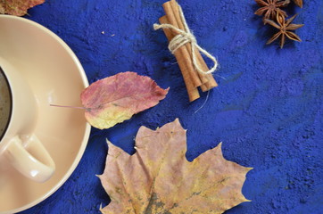 Pumpkin spiced latte or coffee in cup, dry leaves, gifts on dark blue table. Autumn or winter hot drink. Space for text, top view, copy space