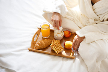 beautiful brunette in a dressing gown and a sweatshirt on her head is having breakfast in bed