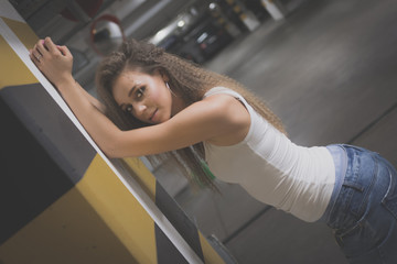 Portrait of young beautiful woman wearing white tank shirt and blue jeans with long hair at underground garage