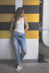 Portrait of young beautiful woman wearing white tank shirt and blue jeans with long hair at underground garage