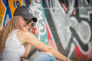 Portrait of young beautiful woman wearing white tank shirt and blue jeans and black hat on brick...