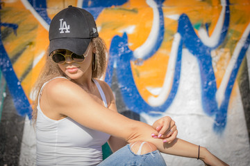 Portrait of young beautiful woman wearing white tank shirt and blue jeans and black hat on brick wall with graffiti background