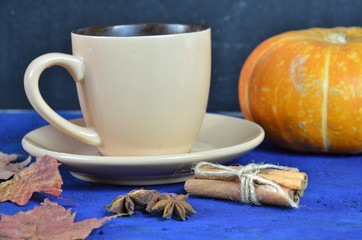 Obraz na płótnie Canvas Pumpkin spiced latte or coffee in cup, dry leaves, gifts on dark blue table. Autumn or winter hot drink. Space for text, top view, copy space