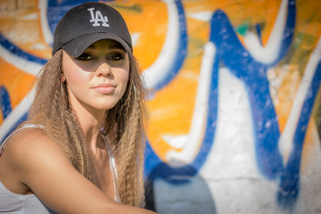 Portrait of young beautiful woman wearing white tank shirt and blue jeans and black hat on brick wall with graffiti background