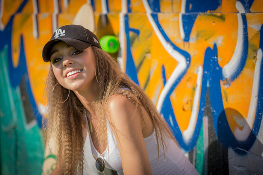 Portrait of young beautiful woman wearing white tank shirt and blue jeans and black hat on brick wall with graffiti background