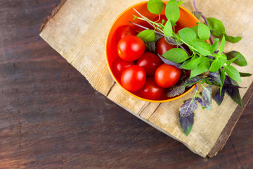 fresh ripe tomatoes ,green and violet basil leavesin a bowl on a wooden cutting board
