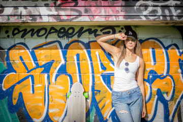 Portrait of young beautiful woman wearing white tank shirt and blue jeans and black hat on brick wall with graffiti background