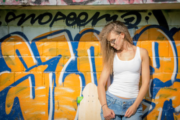 Portrait of young beautiful woman wearing white tank shirt and blue jeans on brick wall with graffiti background