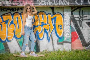 Fototapeta na wymiar Portrait of young beautiful woman wearing white tank shirt and blue jeans on brick wall with graffiti background
