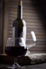 wine glass with expensive red wine,  blurred bottle of wine, wooden background