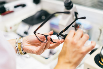 Female optician measuring and preparing glasses on the latest digital device in optical store. Professional ophthalmology instrument in clinic office and optics - obrazy, fototapety, plakaty