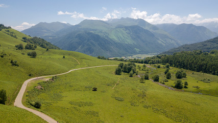 A path between green fields and mountains.