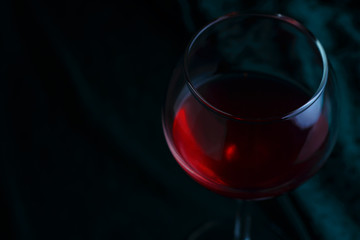 A glass of red wine on a dark velvet-green background