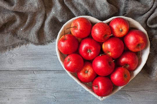 Red apples, basket in the shape of heart on a wooden background