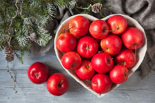 Red apples on a wooden background in a basket in the shape of a heart on a wooden background with branches of a Christmas tree