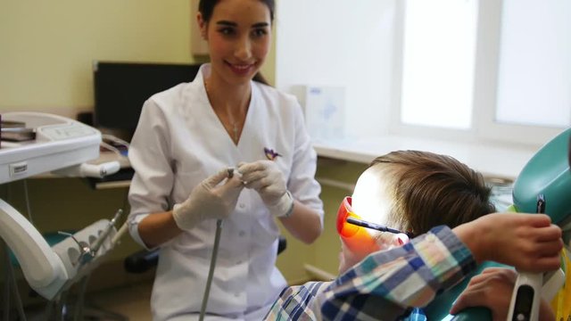 Young dentist prepares for a treatment session. A small patient sits on a chair and waits. His twin brother amuses him.