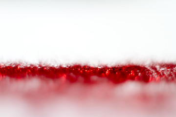 Red glitter texture on white background. Defocused.